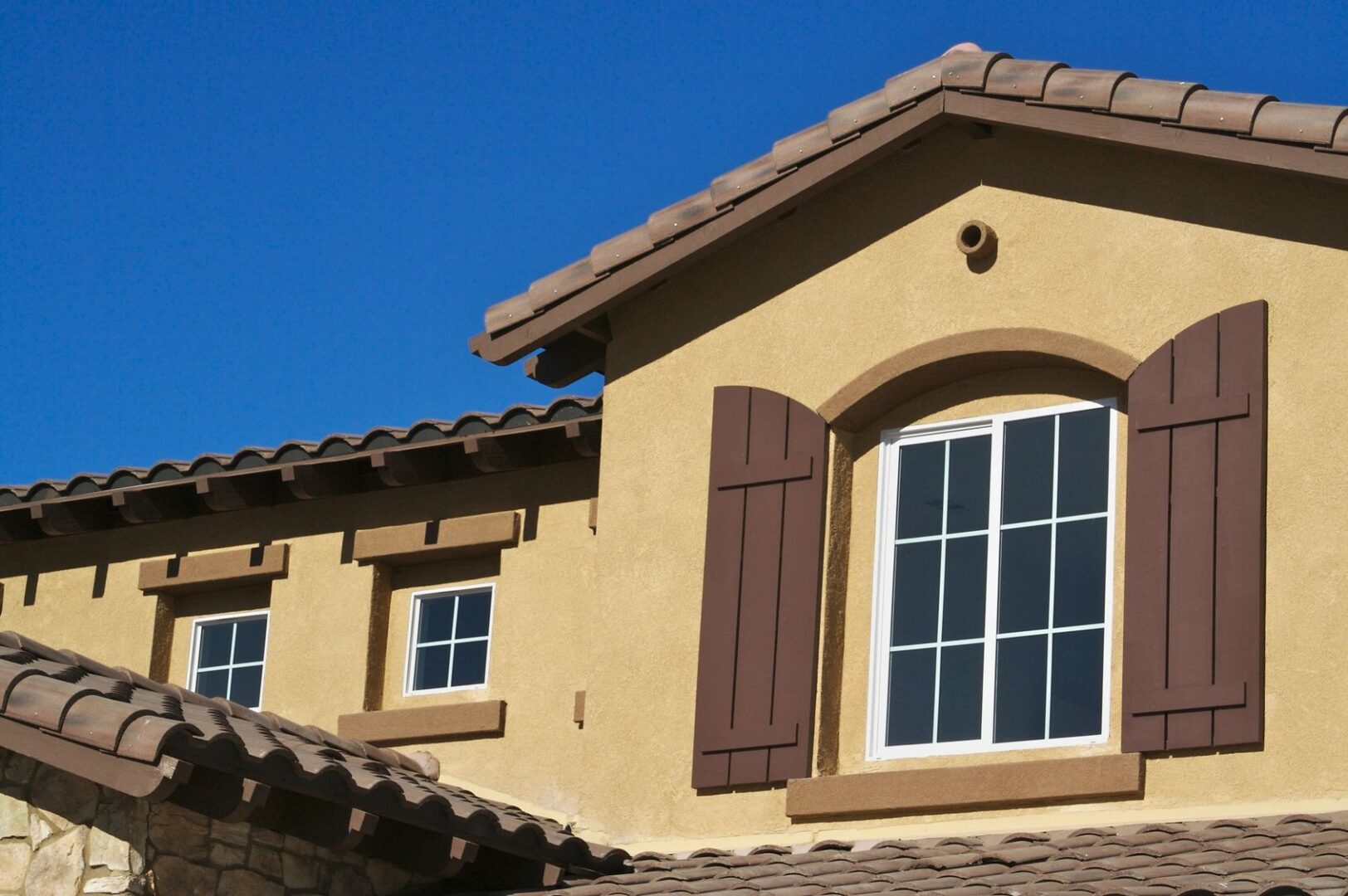 A tan house with brown shutters and windows.