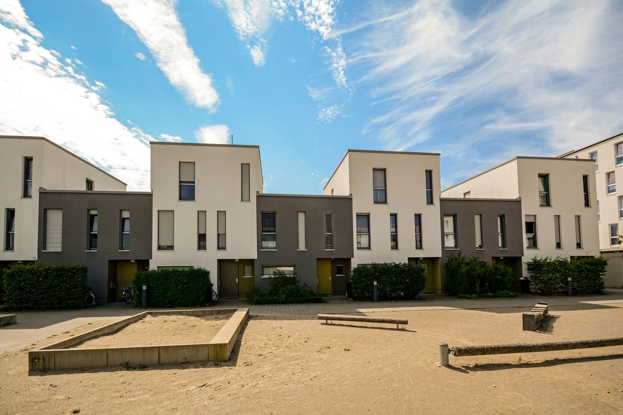 A row of houses on the sand in front of some trees.