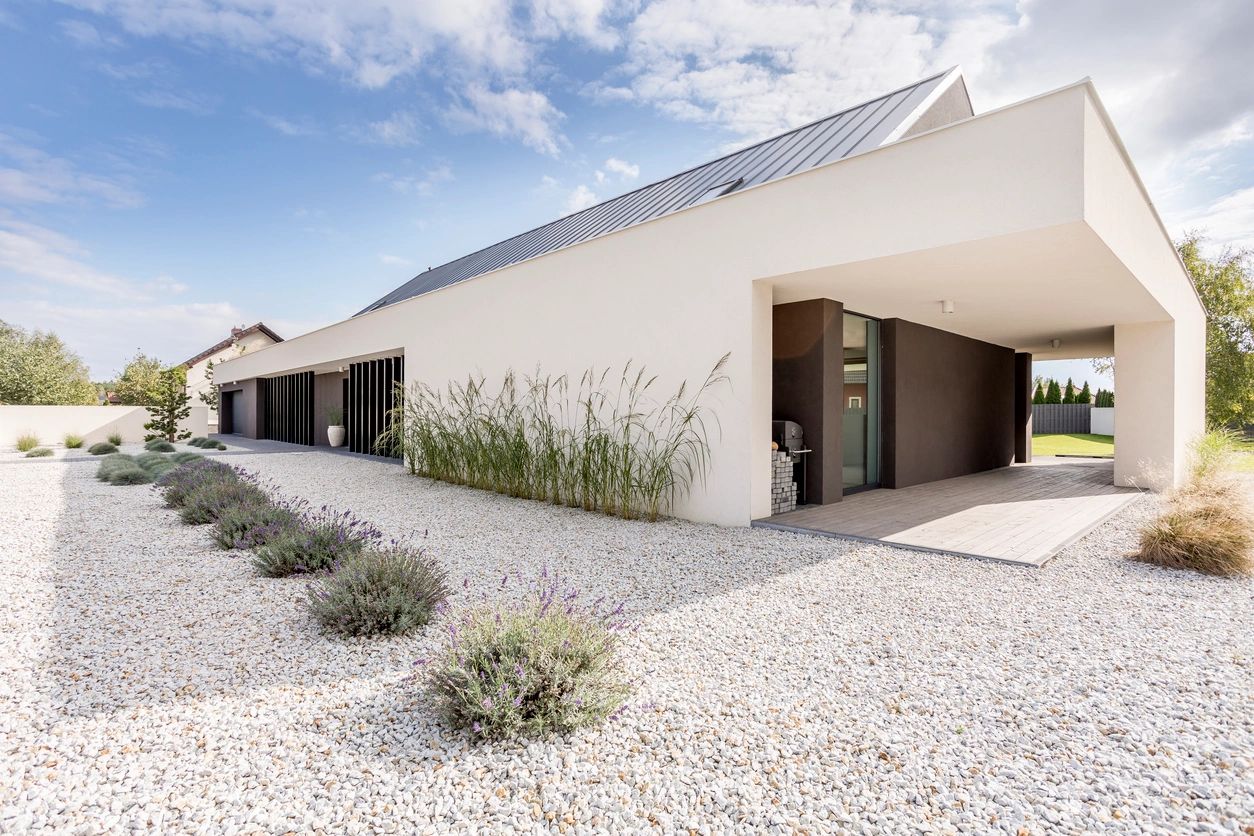 A white building with plants and gravel in the front.